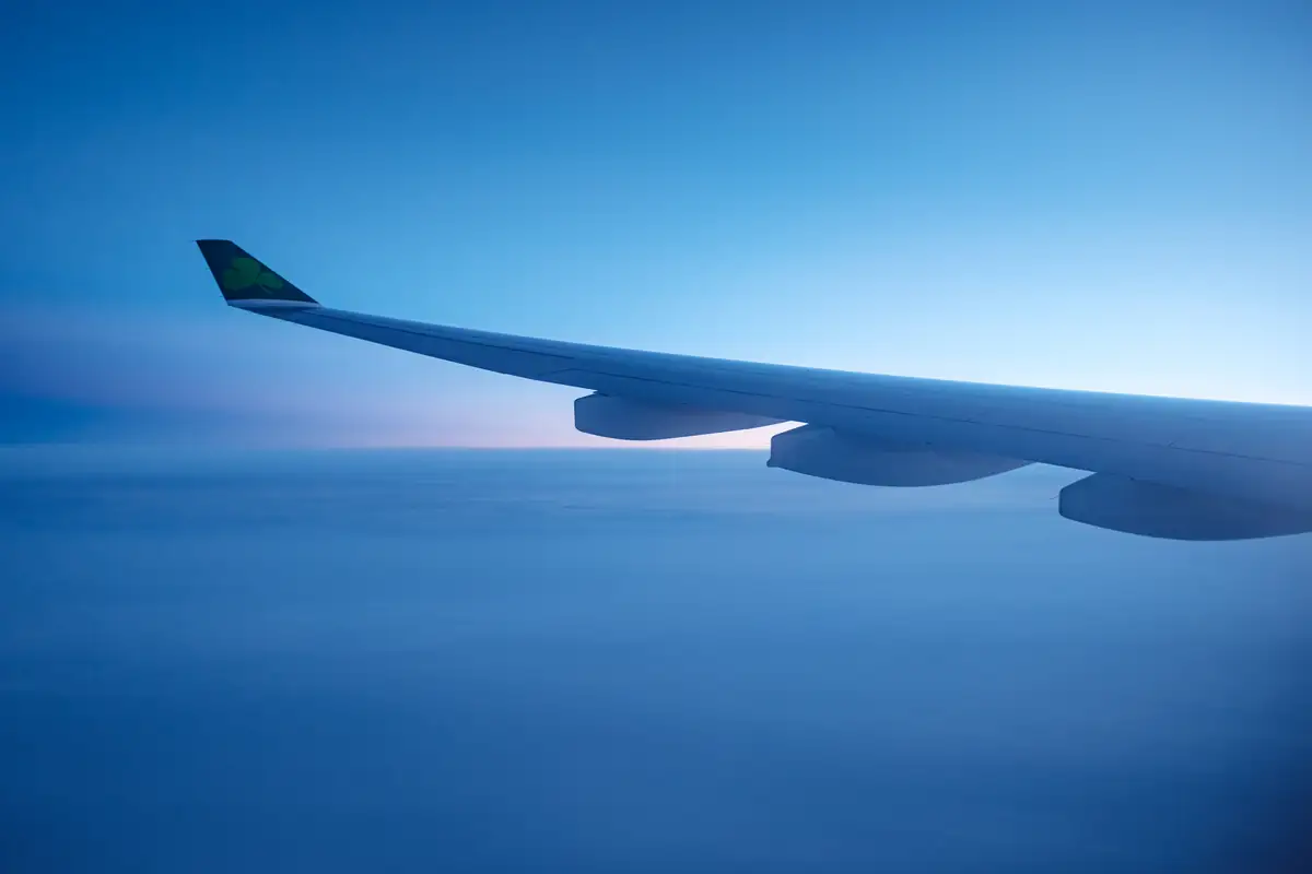 An aircraft wing in flight, in a blue sky above the clouds